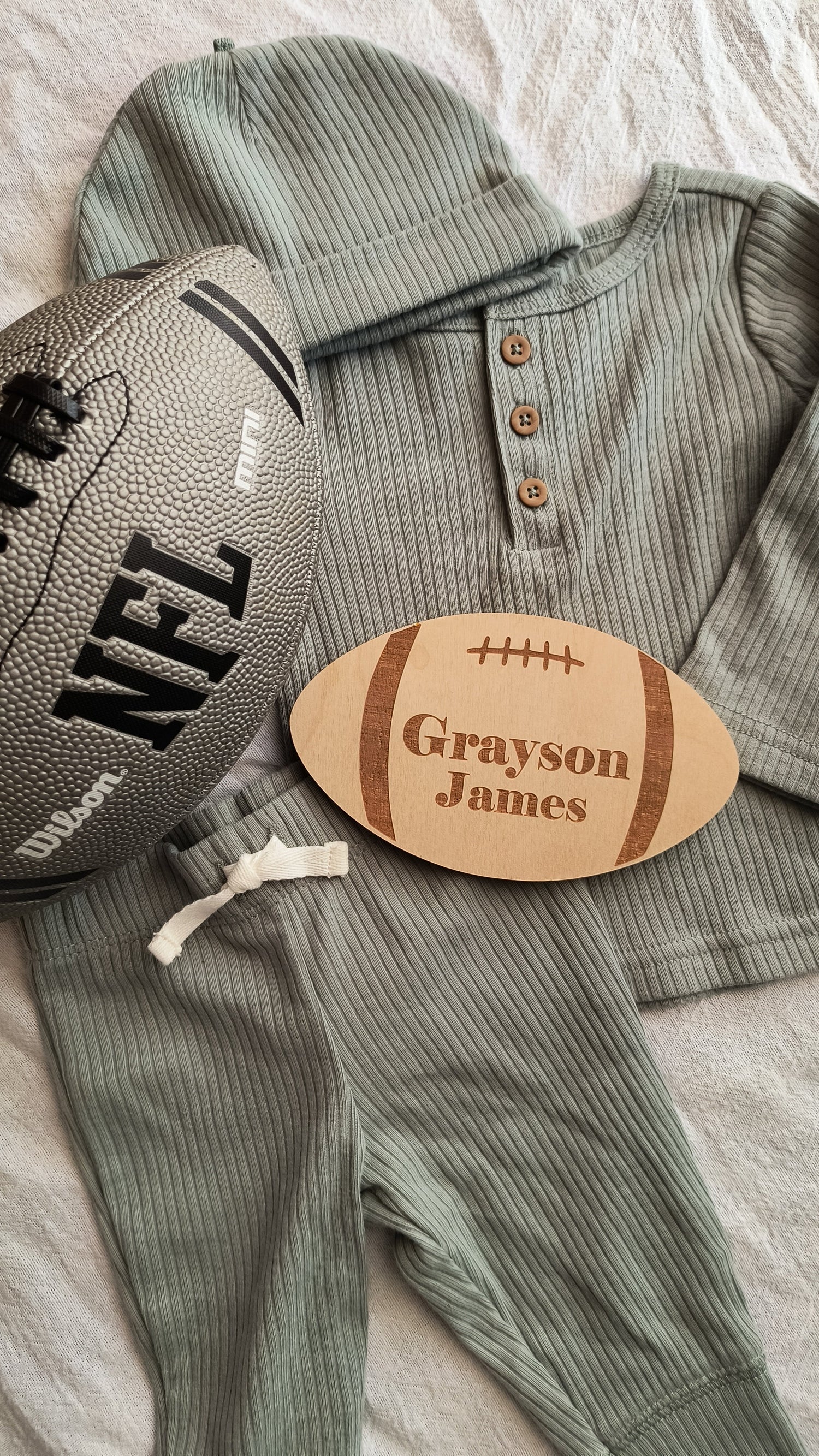 Custom engraved wood football name sign laying on a baby outfit with NFL football laying beside it.