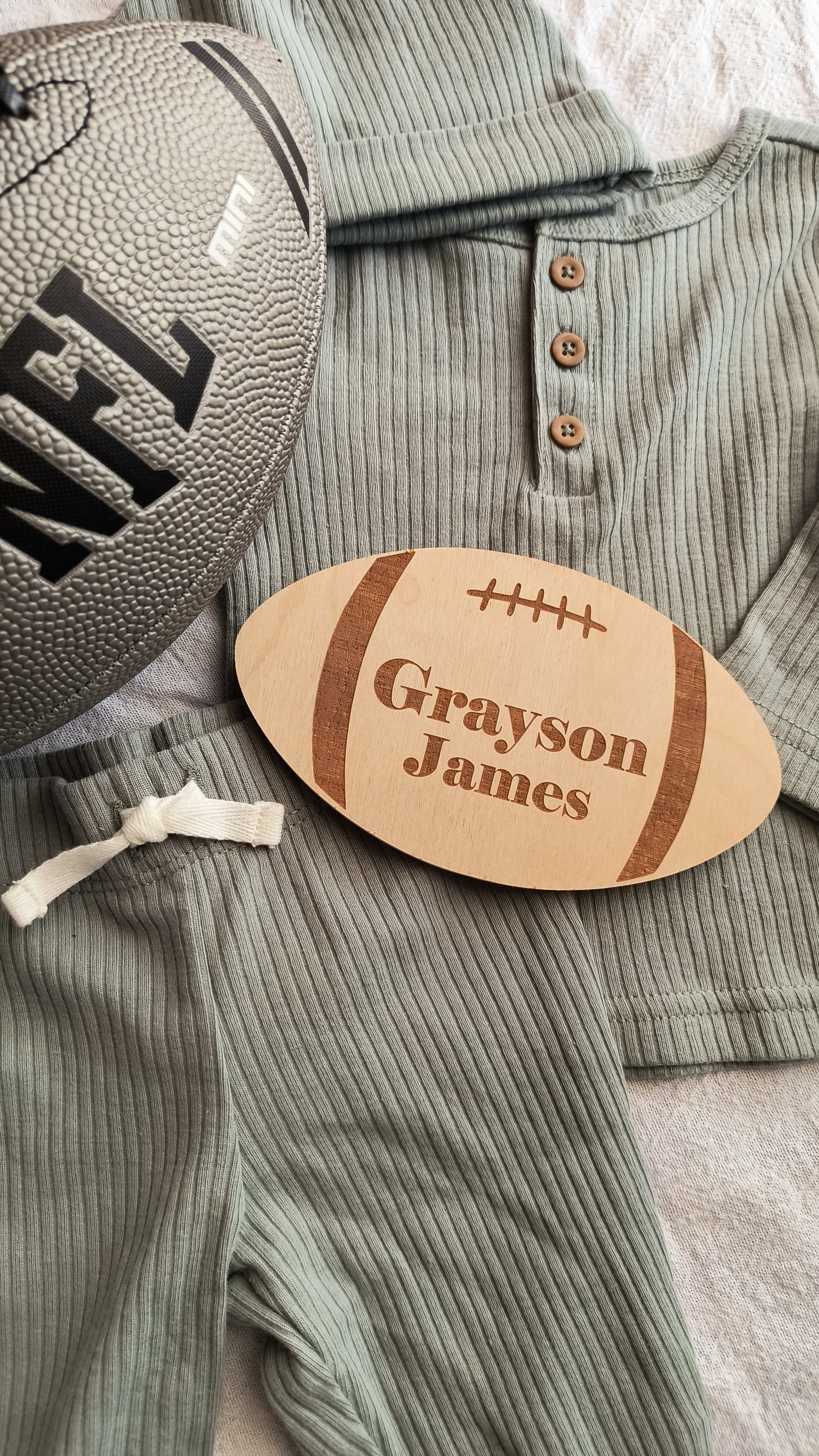 Custom engraved football baby name announcement sign laying on a baby outfit with a NFL football to the left side.