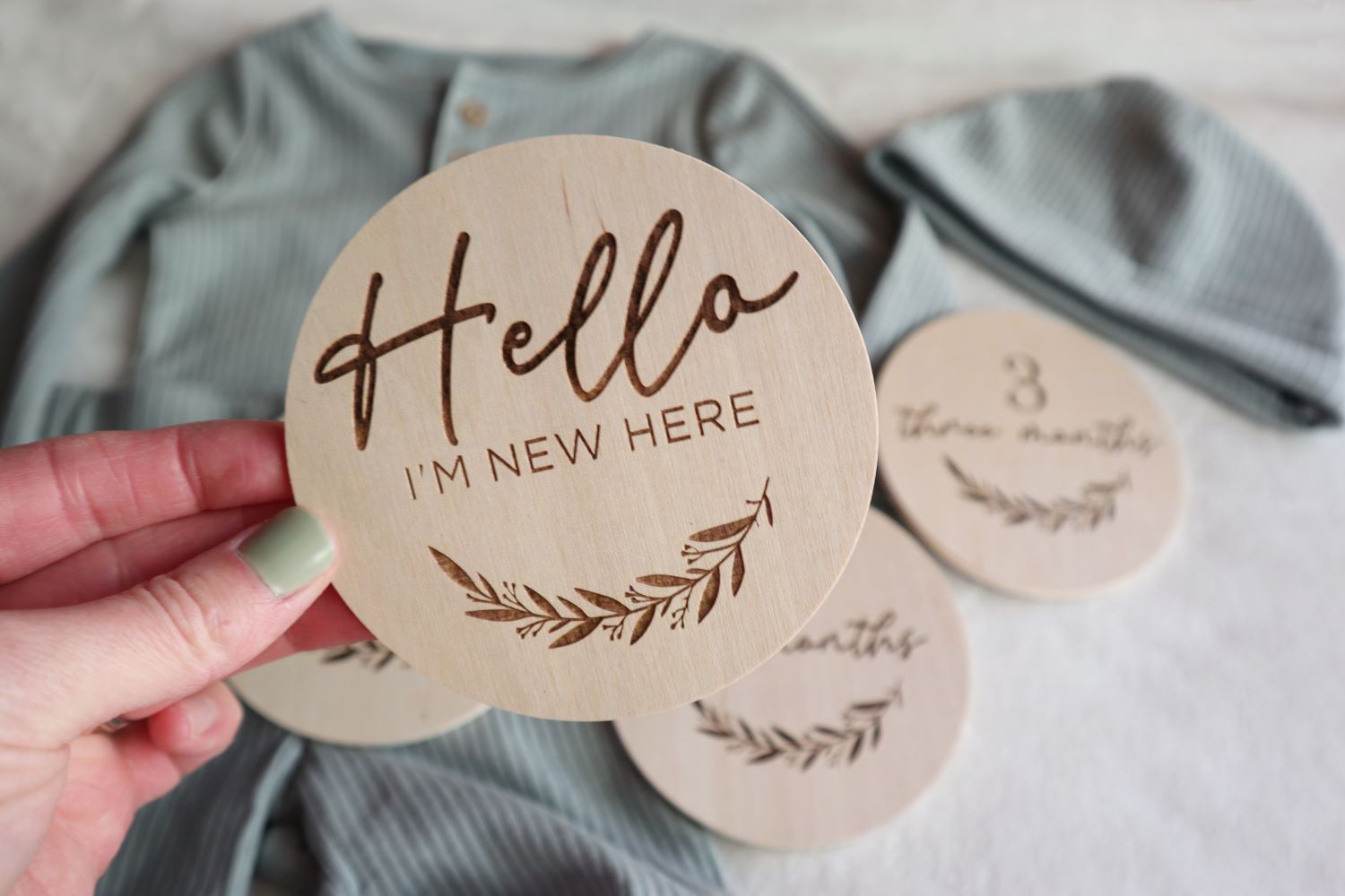 Engraved wood sign set featuring 'Hello, I'm New Here' and monthly milestone signs (1 to 12 months) displayed on a soft baby blanket, ideal for newborn photography.